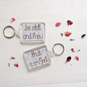 be still and know that i am god bible verse keychain with a pastel splatter pattern behind the words