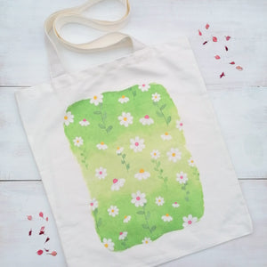 Canvas tote bag with a daisy design at the centre of the tote, painted with watercolours onto a green background.