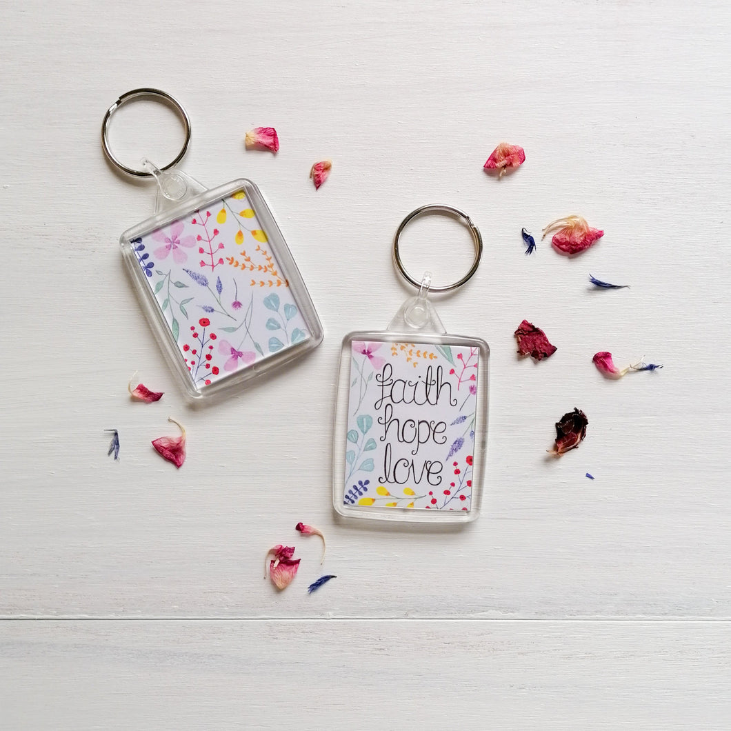 christian keychain with the words faith hope and love lettered at the centre of the keyring with a multicoloured floral design surrounding the verse and on the back of the keychain