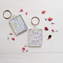 Load image into Gallery viewer, Christian quote keychain with the words god is good lettered at the centre with a watercolour leaf pattern surrounding the words and on the back