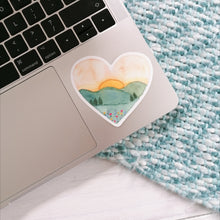 Load image into Gallery viewer, A stunning sunset landscape sticker hand painted into a heart shape. A dreamy design that would make a thoughtful gift to send a loved one as well as a joyful little treat to add to your laptop, water bottle or journal.