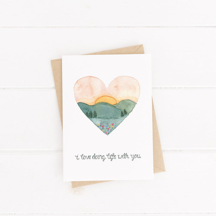 valentines card with the words, I love doing life with you lettered beneath an illustration of a sunset overlooking a field of wildflowers. A stunning card to use for anniversary, valentines or as a love card 