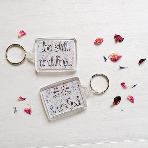 be still and know that i am god bible verse keychain with a pastel splatter pattern behind the words