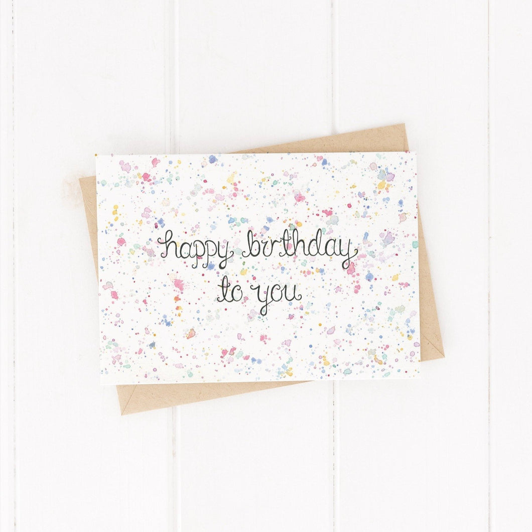 birthday card with a colourful splatter watercolour effect with the words happy birthday to you hand lettered on the birthday card