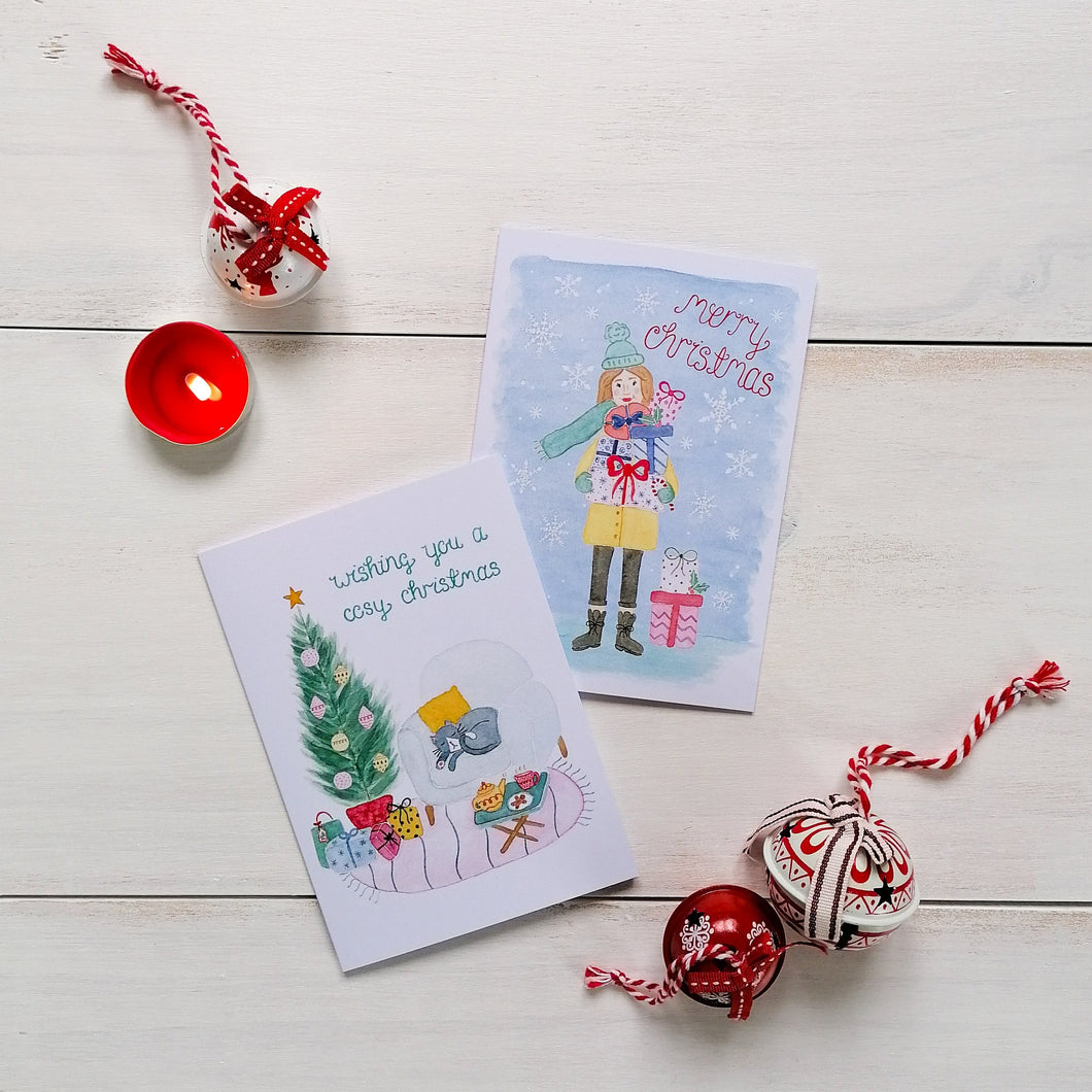set of illustration christmas cards with a cosy cat design and an illustration of a girl carrying gifts in the snow