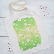 Load image into Gallery viewer, Canvas tote bag with a daisy design at the centre of the tote, painted with watercolours onto a green background.