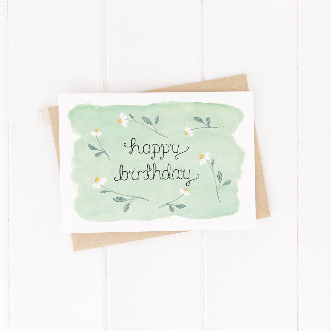Birthday daisy card, with the words happy birthday hand lettered at the centre of the card with a green watercolour background and a daisy pattern surrounding the words, the sweetest birthday card for friends and flower lovers