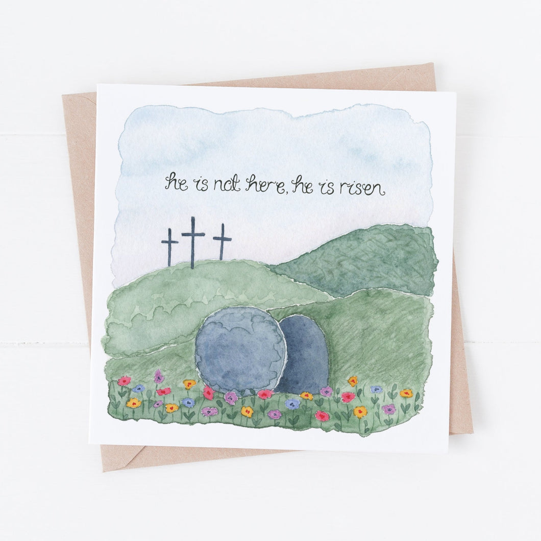 A hand illustrated Easter card with the words from Matthew 28:6, 'he is not here, he is risen' lettered onto a stunning watercolour scene of the stone rolled away from the tomb with the three crosses in the background.