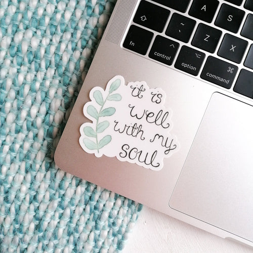 sticker with the words, it is well with my soul with a leaf design placed on a laptop