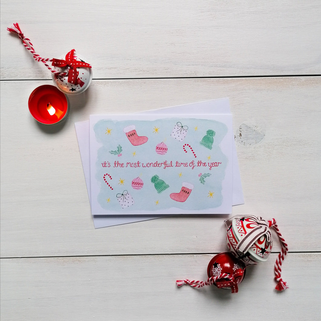 festive christmas card with holly, candy canes, wooly hats and other festive illustrations surrounding the words, it's the most wonderful time of the year