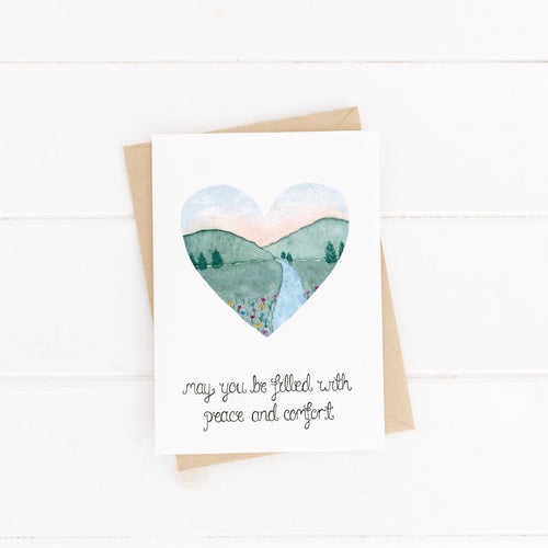 A stunning card with the words 'may you be filled with peace and comfort' hand lettered with a watercolour landscape scene of mountains, a river and wildflowers painted into a heart. The perfect card to share with a loved one during a difficult season.