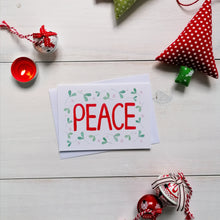 Load image into Gallery viewer, a pretty christmas card with the word peace painted in red at the centre with mistletoe surrounding the word