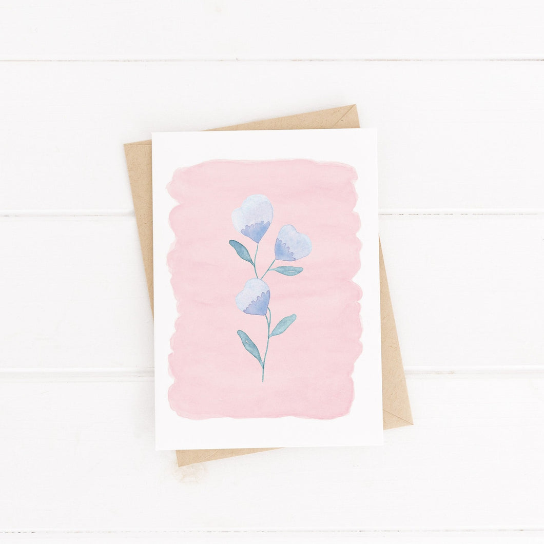A pretty greeting card with a watercolour painted pink background and a dainty purple flower painted on top, a sweet card to fill with kind and encouraging words.
