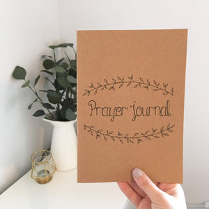 A lovely Christian notebook with the words 'Prayer Journal' lettered at the centre with a dainty leaf wreath drawn around the words.