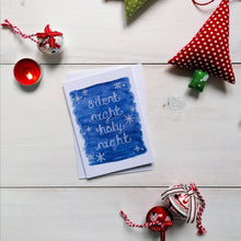 Load image into Gallery viewer, Christmas carol card with the words, silent night holy night lettered in white on a blue background with snowflakes surrounding the word