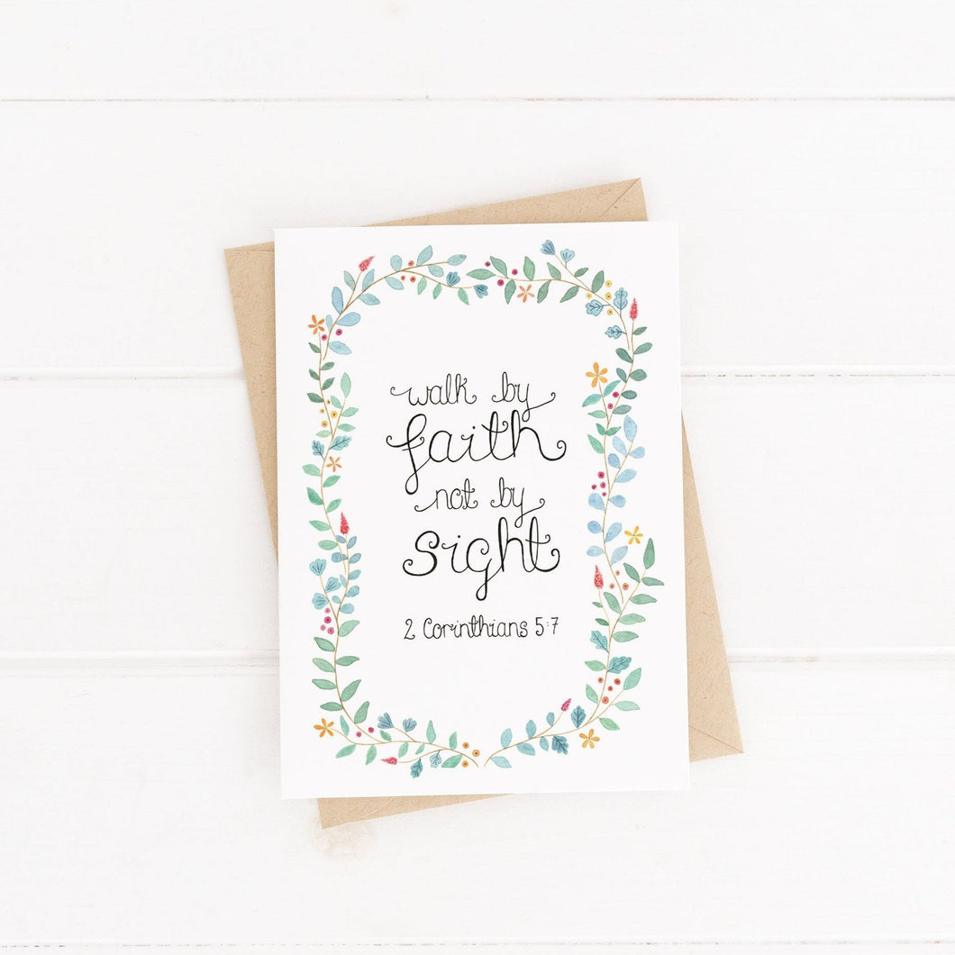 A stunning leaf wreath card with dainty flowers painted around the design with the words from 2 Corinthians 5:7, 'walk by faith, not by sight.' An encouraging Bible verse card to share with a loved one on their baptism, during a difficult time or as a just because.